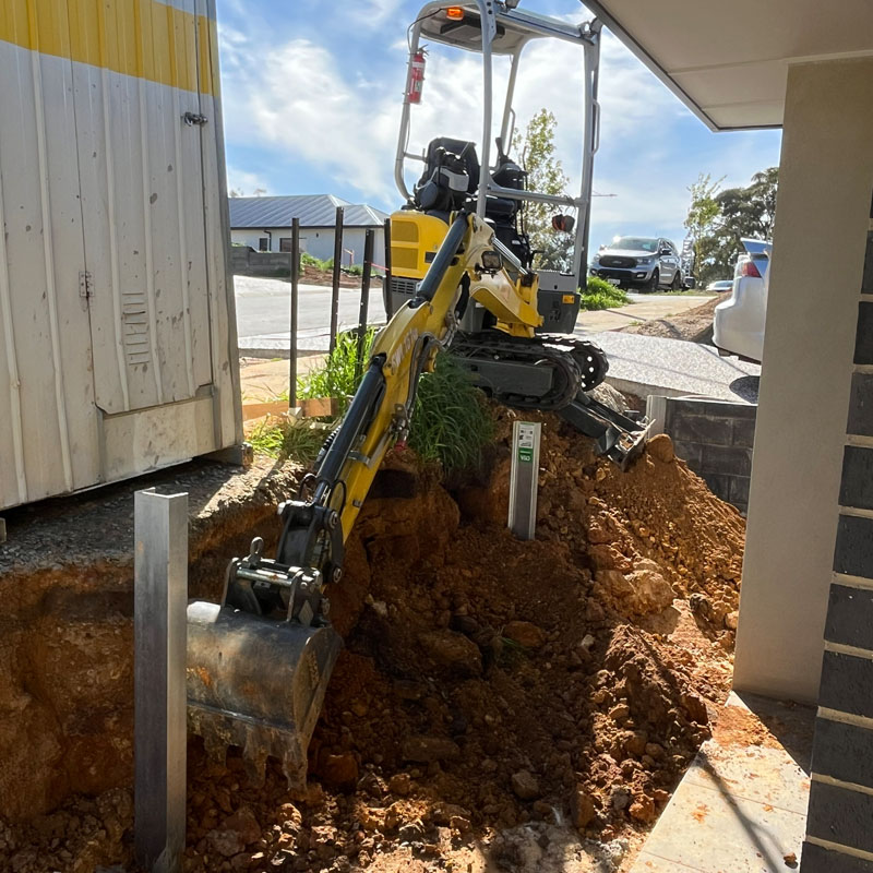 Mini excavator digging beside a new house, with a steel post standing in the hole