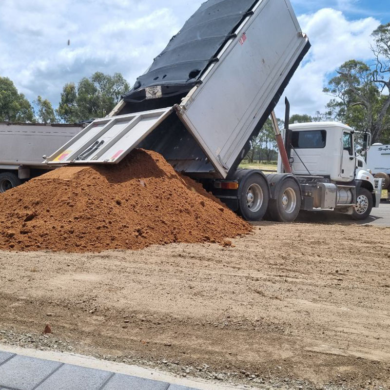 Tipper truck unloading a pile of red soil onto a cleared site